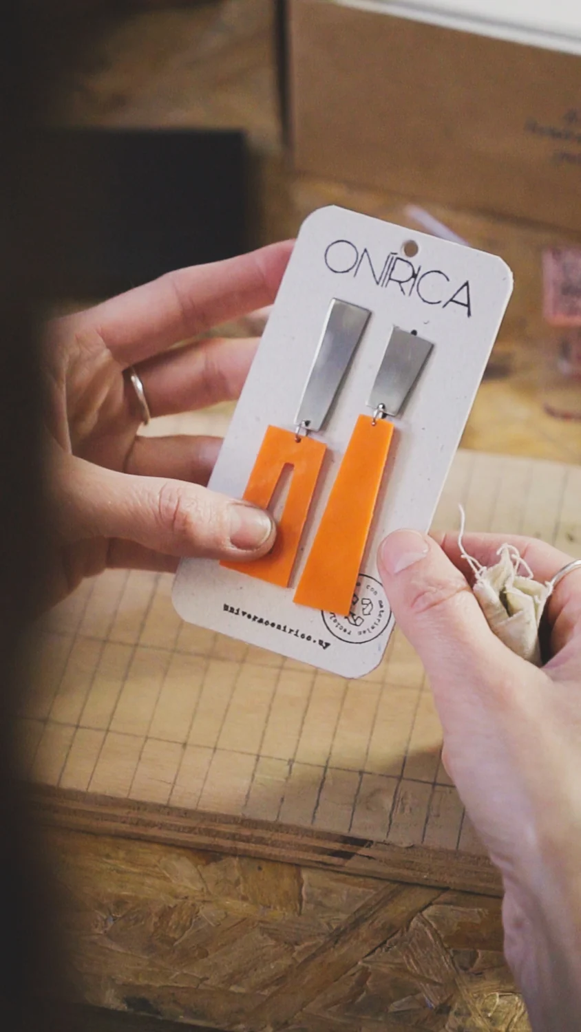 Caravanas ONÍRICA en tonos naranja presentadas sobre su tarjeta de marca